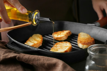 Woman pouring oil on roasting slice of bread, closeup