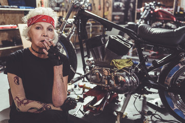 Fototapeta na wymiar Thoughtful old woman smoking next to bike