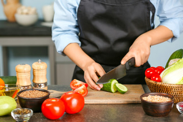 Female hands cutting cucumber at table in kitchen