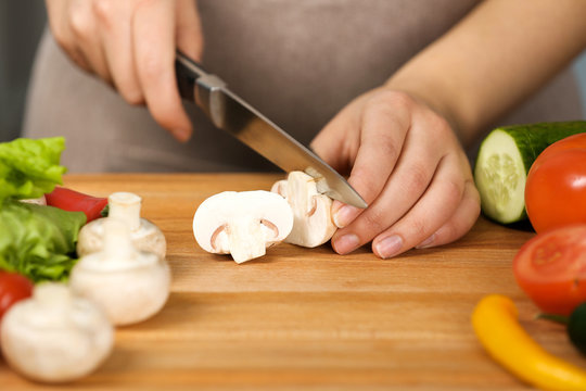 Female hands cutting mushrooms at table in kitchen