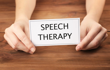 Speech therapy concept. Hands holding card on wooden background