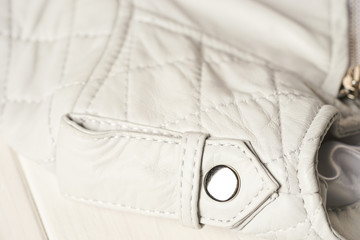 Metal clasp button on white leather jacket.  Leather jacket shoulder detail. White background. Macro detail