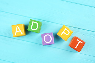 Colorful cubes with word ADOPT on wooden background