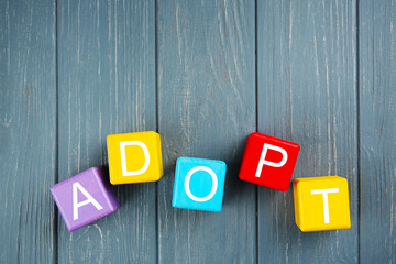 Colorful cubes with word ADOPT on wooden background