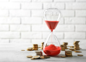 Coins and sandglass on brick wall background