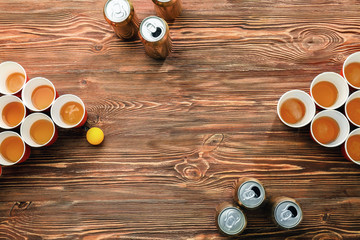 Plastic beer pong cups and cans on wooden table, top view