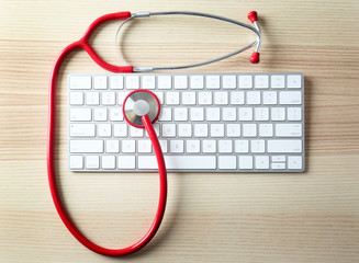 Modern wireless keyboard and stethoscope on light wooden table