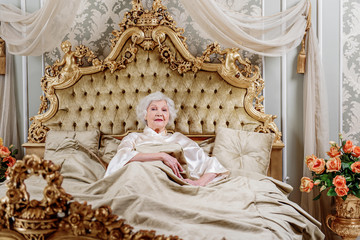 Confident old woman lying on expensive bed