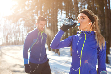 Girl drinks water on training in winter in forest