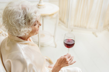 Old lady drinking wine at home