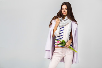 Fashion photo of a beautiful young woman with tulips in her hand .she dressed  in a beautiful coat, scarf, pants and T-shirt with stripes.Spring concept. March 8. beautiful girl in stylish clothes.
