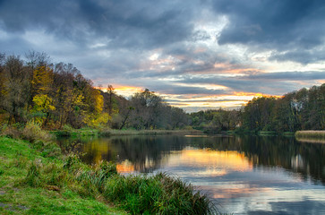 Sunset on the lake with forest with green grass in summer.