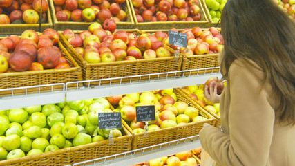 Woman selecting fresh red apples in grocery store produce department and putting it in plastic bag. Young pretty girl is choosing apples in supermarket and putting them into shop basket. Close up