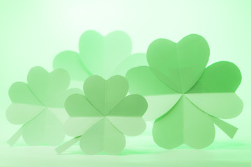 Hand made 4 paper four-leaf clovers on soft green light background.