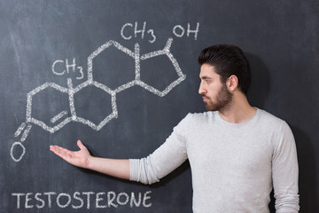 chemical structure of testosterone molecule drawn on chalkboard background with man in front of it - obrazy, fototapety, plakaty