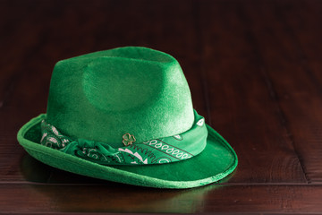 A green suede fedora hat with bandana and clover pin on the rustic wooden table.