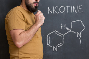 Nicotine molecule chemical structure on blackboard. Chemical structure of nicotine from cigarettes written on blackboard with man beside smoking electric cigarette - obrazy, fototapety, plakaty