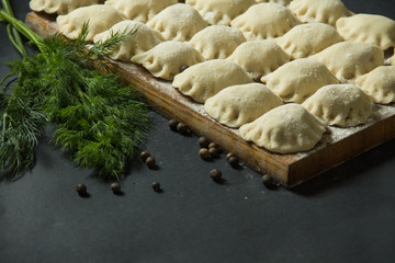 dumplings on a black background with fresh herbs and vegetables. homemade food. Traditional Russian food is pelmeni.