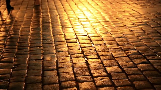 People walking on a cobblestone street  by colourful neon street lights