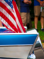 Detail of a classic car with an American flag attached driving in a Fourth of July Parade.
