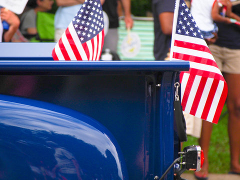 American flags attached to a bright blue classic truck driving in a Fourth of July parade.