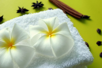 Obraz na płótnie Canvas White towel with flowers of plumeria with stars of anise and cinnamon sticks on the yellow background for spa theme.