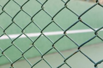 Closeup view of a fence with a blurred tennis court background.
