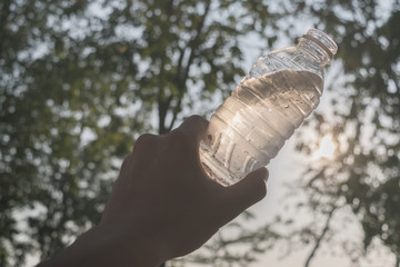 Hand holding a bottle of clean water visor sunlight in the park.