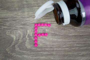 Pink pills forming shape to F alphabet on wood background