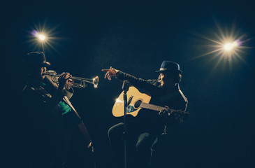 Musician Duo band playing a Trumpet and singing a song and playing the guitar on black background with spot light and lens flare, musical concept