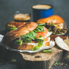 Bagel with salmon, avocado, cream-cheese, basil, espresso coffee, capers on rustic wooden board over dark background, selective focus, square crop. Healthy or diet bkeakfast concept