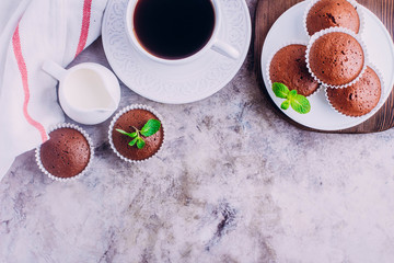 Obraz na płótnie Canvas Homemade chocolate muffins and white cup of coffee on gray table background. Mini cakes for breakfast. Top view with copy space
