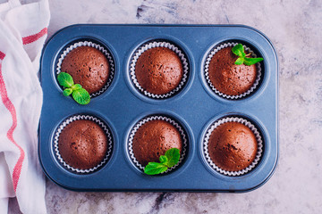 Homemade chocolate muffins in metal mold for baking on gray table background. Mini cakes for breakfast. Top view