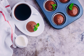 Homemade chocolate muffins and white cup of coffee on gray table background. Mini cakes for breakfast. Top view with copy space