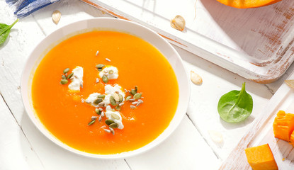 Pumpkin and carrot soup with cream and seeds on white wooden background.