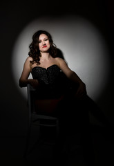 Sexy girl in lacy lingerie and corset, sitting on chair posing in the studio a dark background