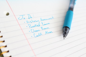 To do list written in blue ink on lined paper with a pen