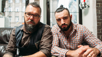 Hipster and biker sitting together portrait. Two bearded men with different hobbies, but similar style. Generation, trend, subculture, fashion, lifestyle concept