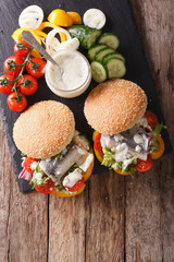 Fishburger with herring, gravy and fresh vegetables close-up. vertical top view