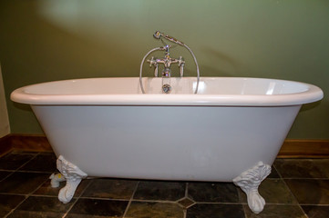 Old type modern replica of a white footed bath tub in olive green bathroom