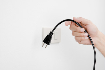 Hand of man unplug electric outlet plug on wall white background safety concept - obrazy, fototapety, plakaty