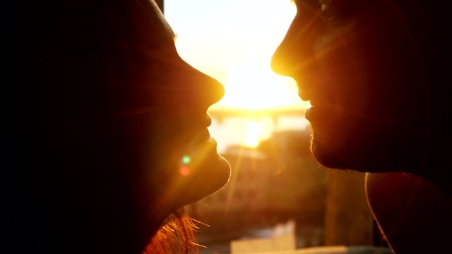Romantic young couple silhouette is kissing looking each other on a sunset with sun shining bright behind them on a horizon with lense flare effects. 3840x2160