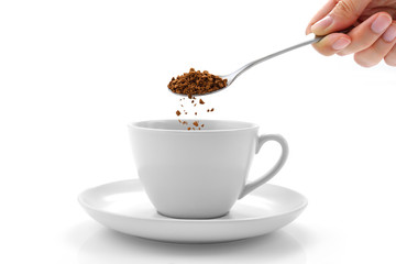 Hand pours instant coffee from a spoon in a coffee cup