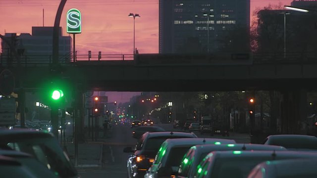 Berlin in the evening , red sky , large intersection with traffic , a train crosses .its a rush hour.
