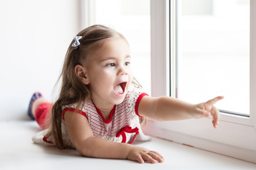 Little smiling child girl watching out the window