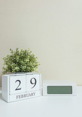 White wooden calendar with black 29 february word with clock and plant on white wood desk and cream wallpaper textured background in selective focus at the calendar
