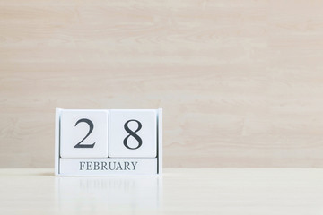 Closeup surface white wooden calendar with black 28 february word on blurred brown wood desk and wood wall textured background with copy space in selective focus at the calendar