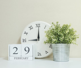 White wooden calendar with black 29 february word with clock and plant on white wood desk and cream wallpaper textured background in selective focus at the calendar