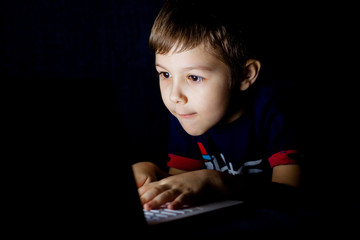 Little boy doing homework on the computer in the dark night. Child to play the game on a laptop.