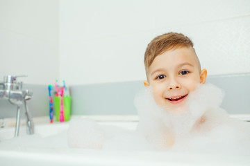 Happy young boy taking a bath. Smiling child washes in the foam.